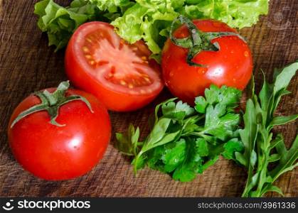 Juicy tomatoes with green-stuff on wooden table