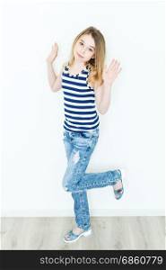 Jumping cute girl eleven years old with blond long hair standing near white wall and upwards hands