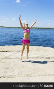 Jumping girl on the riverbank in pink swimsuit