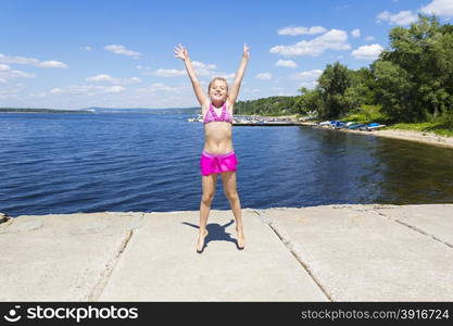 Jumping girl on the riverbank in pink swimsuit