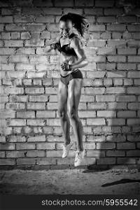 Jumping muscular woman on grey brick wall (monochrome version)