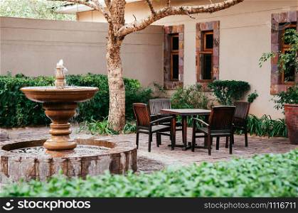 JUN 19, 2011 Serengeti, Tanzania - - Fountain and old wooden chairs and table set in tropical backyard garden under tree with green shrubs under natural light in the afternoon