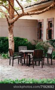 JUN 19, 2011 Serengeti, Tanzania - - Old wooden chairs and table set in tropical backyard garden under tree with green shrubs under natural light in the afternoon