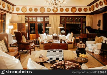 JUN 20, 2011 Serengeti, Tanzania - Luxury African Safari lodge interior with vintage white armchairs, sofa couch wooden table and grand piano under warm light with antique decoration