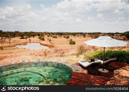 JUN 20, 2011 Tanzania - Swimming pool African Luxury Safari lodge terrace with white umbrella and pool bed in Savanna forest of Serengeti Grumeti wildlife Reserve.