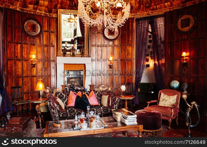 JUN 23, 2011 Ngorongoro, Tanzania - Luxury African tribal cottage living room interior decoration with old vintage colonial style wooden furnitures, armchair, sofa and tables under warm light from grand chandelier