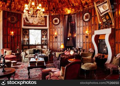 JUN 23, 2011 Ngorongoro, Tanzania - Luxury African tribal cottage living room interior decoration with old vintage colonial style wooden furnitures, armchair, sofa and tables under warm light from grand chandelier