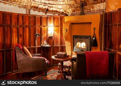 JUN 23, 2011 Ngorongoro, Tanzania - Luxury African tribal hut interior decoration with old vintage wooden furnitures, leather chair under warm light and antique fireplace.