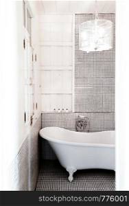 JUN 7, 2012 Hua Hin, THAILAND - Vintage warm cozy clean style bathroom with bathtub and pedant lamp, mosaic tiles floor with natural light shot througe white door frame