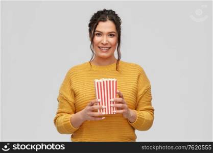 junk-food and people concept - happy smiling young woman with pierced nose holding bucket of popcorn over grey background. happy smiling young woman with bucket of popcorn