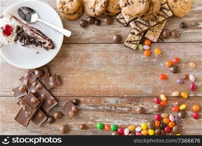 junk food, sweets and unhealthy eating concept - close up of chocolate, drop candies and piece of cake and cookies on wooden table. close up of different sweets on table