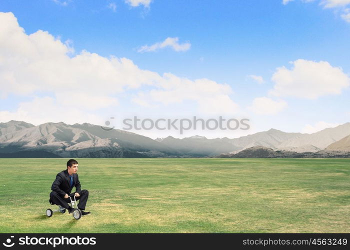 Just like a child. Young funny businessman riding three wheeled bicycle