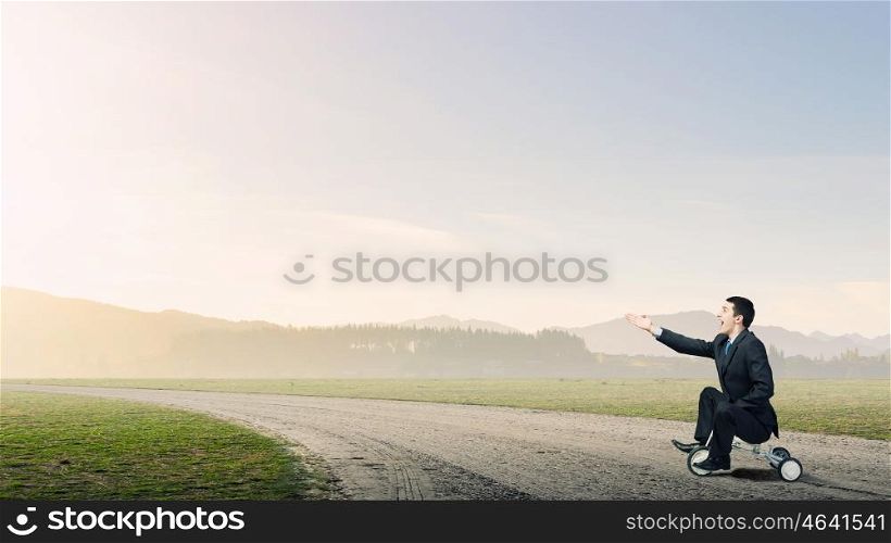 Just like a child. Young funny businessman riding three wheeled bicycle