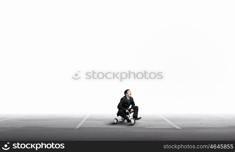 Just like a child. Young funny businessman riding three wheeled bicycle