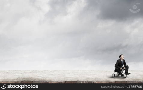 Just like a child. Young funny businessman riding three wheeled bicycle