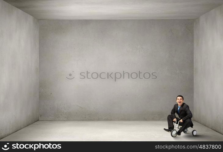 Just like a child. Young funny businessman riding three wheeled bicycle