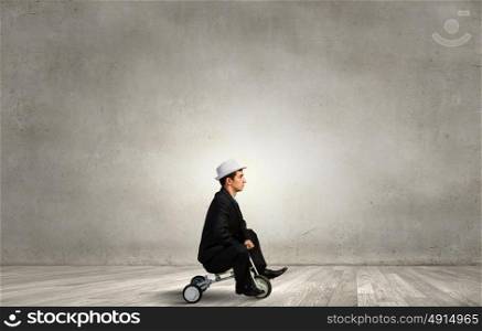 Just like a child. Young funny businessman riding three wheeled bicycle
