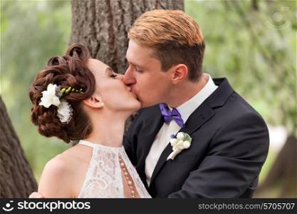Just married couple kissing between tree trunks and pond&#xA;