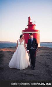 Just married couple walking against a lighthouse at sunset