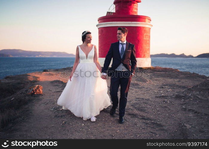 Just married couple walking against a lighthouse at sunset