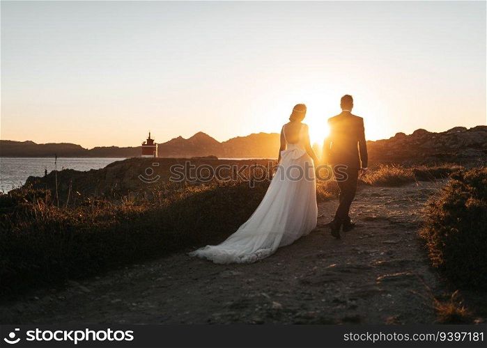 Just married couple walking towards a lighthouse at sunset
