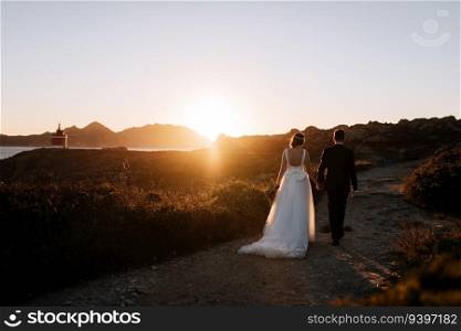 Just married couple walking towards a lighthouse at sunset
