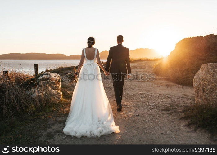 Just married couple walking towards the ocean at sunset