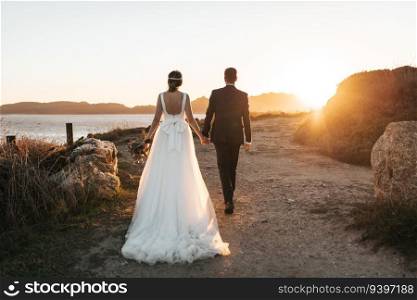 Just married couple walking towards the ocean at sunset