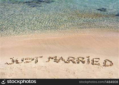 Just Married written in sand on a beautiful beach, blue clear waves in background