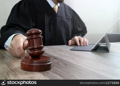 justice and law concept.Male judge in a courtroom striking the gavel,working with digital tablet computer docking keyboard on wood table