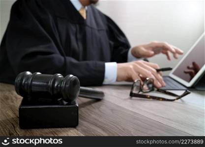 justice and law concept.Male judge in a courtroom with the gavel,working with digital tablet computer docking keyboard on wood table,eyeglass