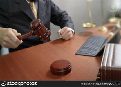 justice and law concept.Male judge in a courtroom with the gavel,working with smart phone,digital tablet computer docking keyboard,brass scale,on wood table