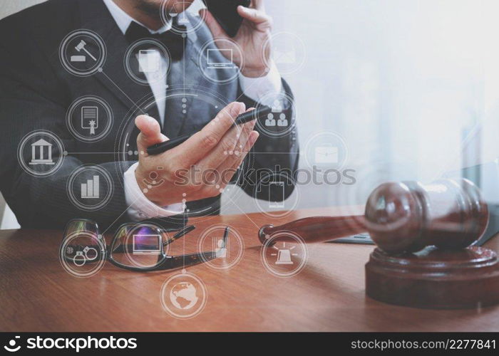 justice and law concept.Male lawyer in office with the gavel,working with smart phone,digital tablet computer docking keyboard,brass scale,on wood table,virtual interface graphic icons diagram