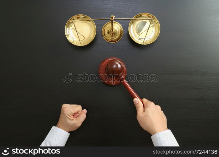 justice and law concept.Top view of Male judge hand in a courtroom with the gavel and brass scale on dark wood table