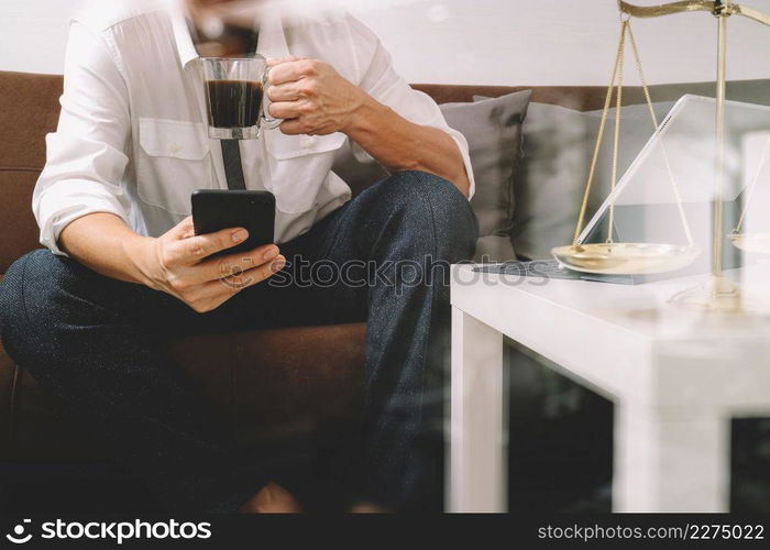 Justice and Law context.Male lawyer hand sitting on sofa and working with smart phone,digital tablet computer docking keyboard with gavel and document on living table at home,filter effect