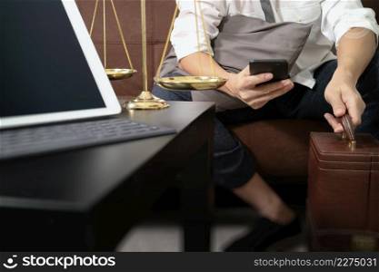 Justice and Law context.Male lawyer hand sitting on sofa and working with smart phone,digital tablet computer docking keyboard with gavel and document on living table at home