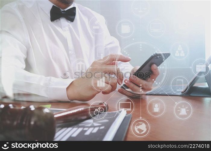 Justice and Law context.Male lawyer hand working with smart phone,digital tablet computer docking keyboard with gavel and document on wood table,virtual interface graphic icons diagram