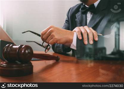 Justice and Law context.Male lawyer hand working with smart phone,digital tablet computer docking keyboard with gavel and document on wood table,filter effect