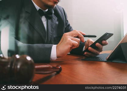 Justice and Law context.Male lawyer hand working with smart phone,digital tablet computer docking keyboard with gavel and document on wood table,filter effect