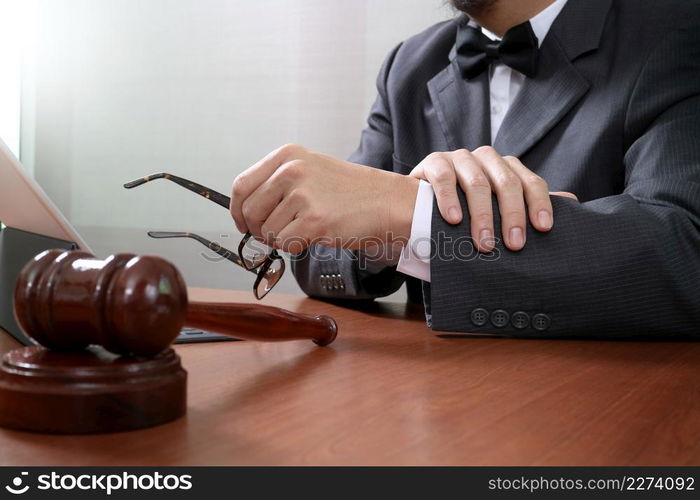 Justice and Law context.Male lawyer hand working with smart phone,digital tablet computer docking keyboard with gavel and document on wood table