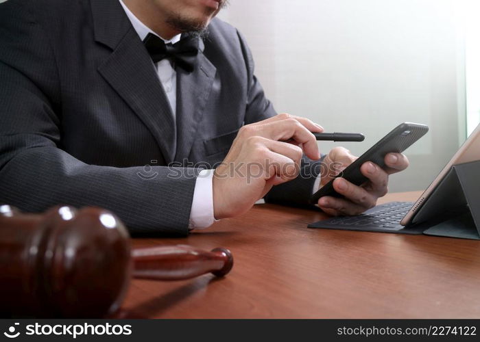 Justice and Law context.Male lawyer hand working with smart phone,digital tablet computer docking keyboard with gavel and document on wood table