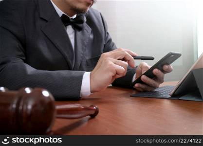 Justice and Law context.Male lawyer hand working with smart phone,digital tablet computer docking keyboard with gavel and document on wood table
