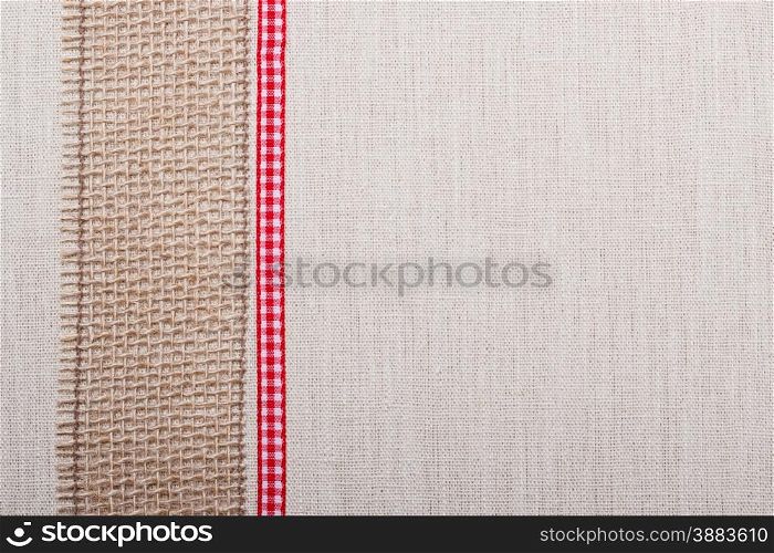 Jute mesh and red ribbon on bright fabric textile material, natural linen background