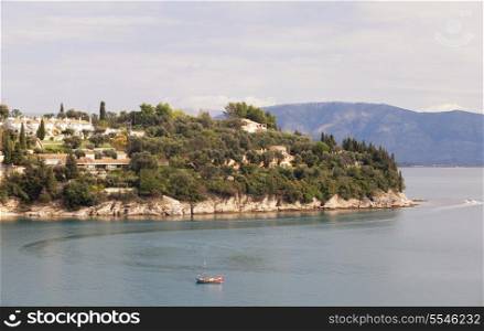 Kalami bay, Corfu, seen from the south side, with new holiday villas on the cliff and a traditional fishing boat at work. Kalami is famous for Lawrence Durrell&rsquo;s book about his time here in the 1930s
