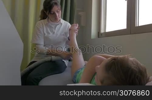 KALIKRATIA, GREECE - JANUARY 12, 2016: Child is under physiotherapy treatment in Evexia clinic. Therapist affecting calf muscles with special equipment