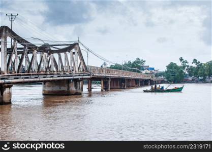 Kampot, Cambodia ? SEPTEMBER 22, 2013: Landscape orientation view, couple fisherman with old fishing boat pass under the old French bridge over the Praek Tuek Chhu River. Kampot Province.