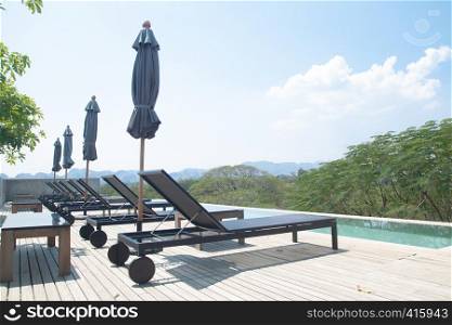 Kanchanaburi, Thailand - February 20, 2019 : Modern and simply design chaise lounge and swimming pool on the hotel roof top with mountain view