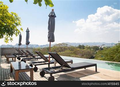 Kanchanaburi, Thailand - February 20, 2019 : Modern and simply design chaise lounge and swimming pool on the hotel roof top with mountain view