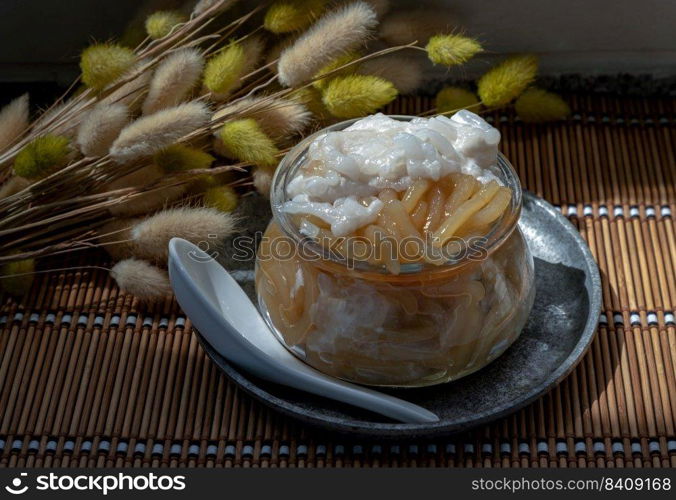 Kanom pla krim khai tao or Sweet rice noodles with coconut cream in glass bowl served with white spoon. Traditional thai dessert, Copy space, Selective focus.