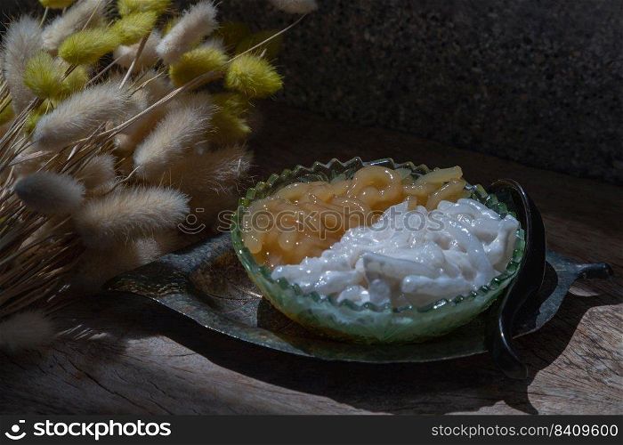 Kanom pla krim khai tao or Sweet rice noodles with coconut cream in glass bowl served with black spoon. Traditional thai dessert, Copy space, Selective focus.